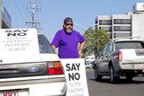 A man stands beside his car with a sign reading "say no to chashless welfare".