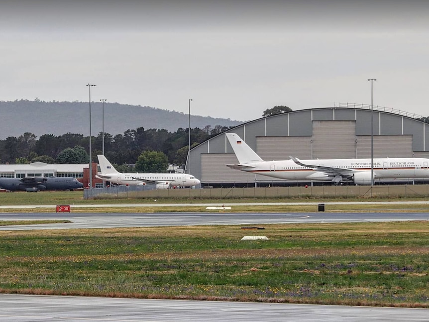 Three planes behind a fence on the tarmac at an airport.