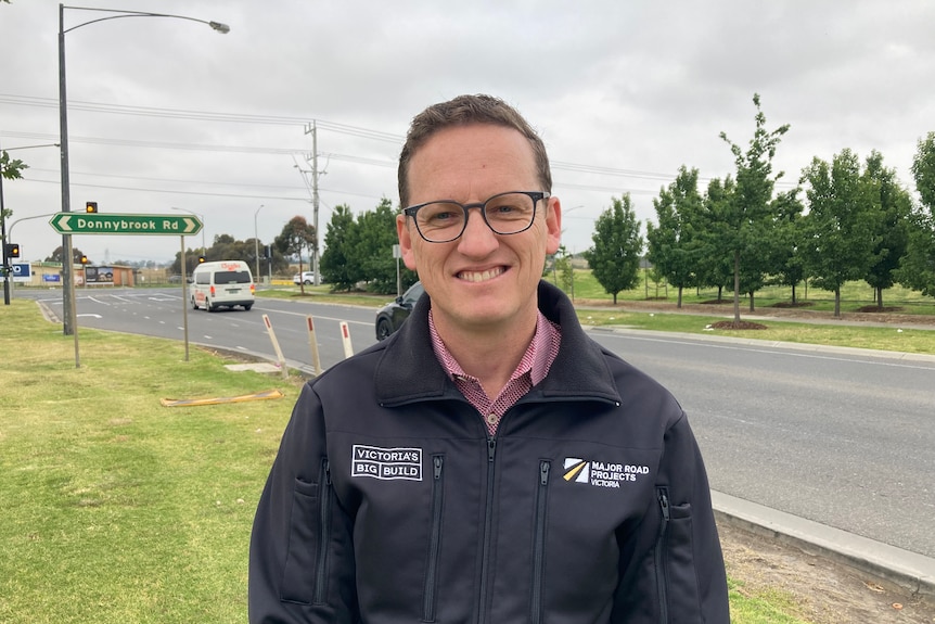 Adrian Furner smiles wearing a work jacket near a road, with a sign for Donnybrook Road in the background.