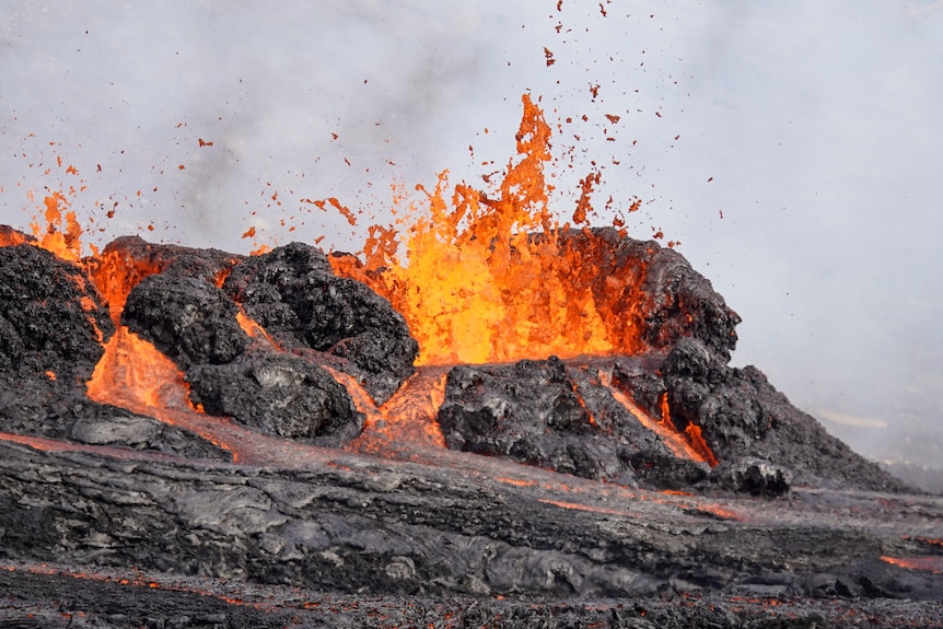 검은 암석에서 빛나는 붉은 용암이 분출하는 동안 다른 분출의 흐름이 쏟아집니다. 