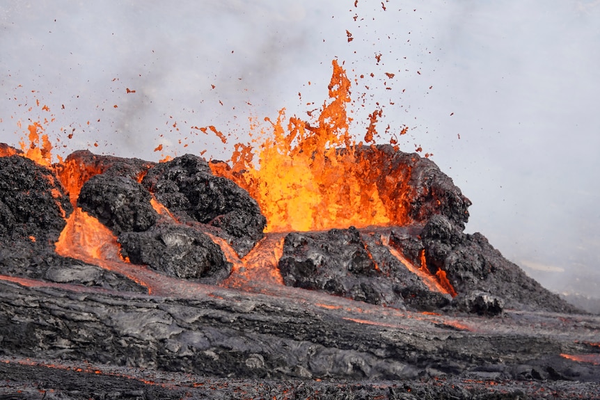 Glowing red lava explodes out of black rock as other streams flow from the explosion. 