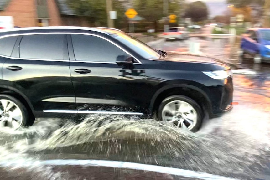 A car drives through a flooded street. 