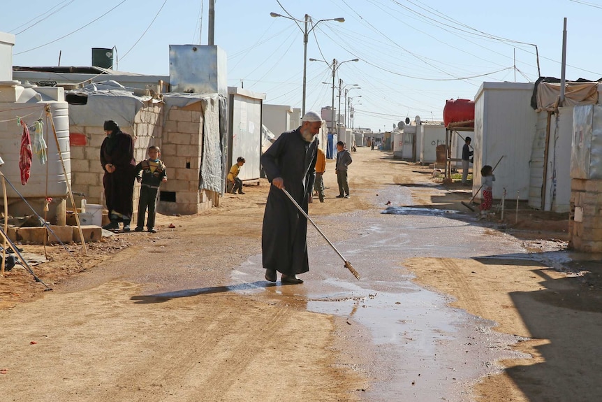 A man stand next to a puddle on a dirt track between tents.