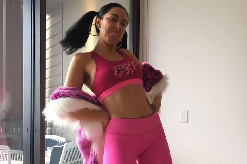 A woman in a pink work out outfit, tights and a small crop top, a torso tattoo visible