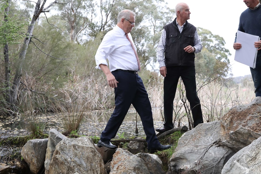 PM Scott Morrison leans backwards as he awkwardly walks over rocks next to a pond