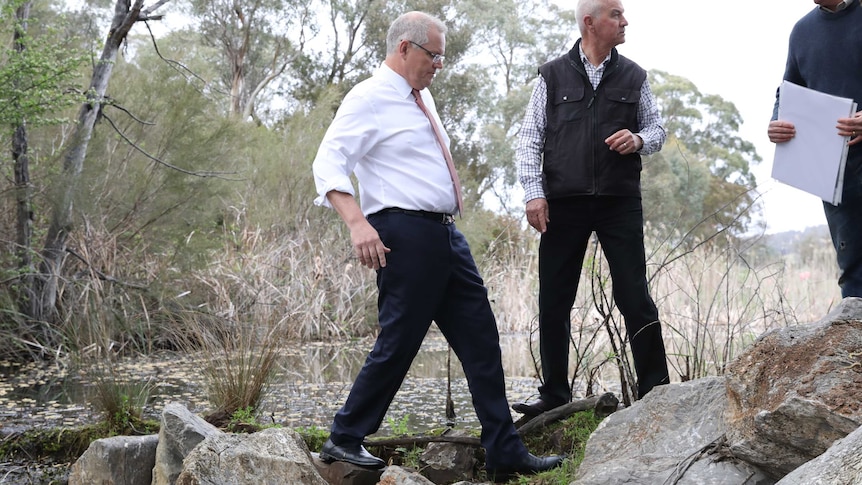 PM Scott Morrison leans backwards as he awkwardly walks over rocks next to a pond