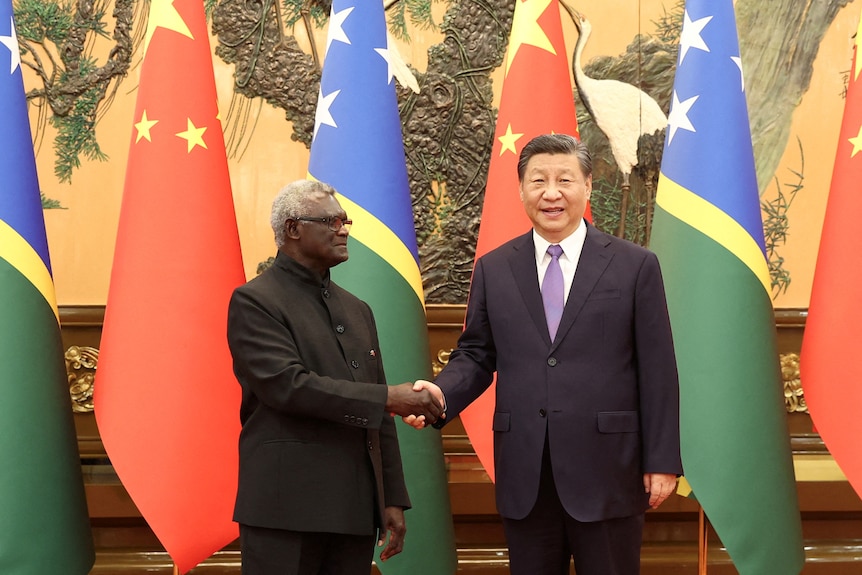 two men shake hands with red china and blue green solomon islands flags in the background