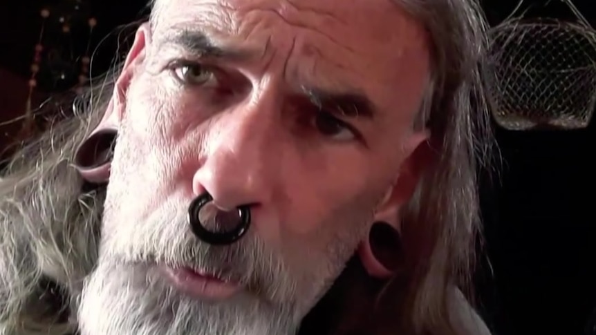 A man with stretchers, a septum ring and long grey hair and a beard.