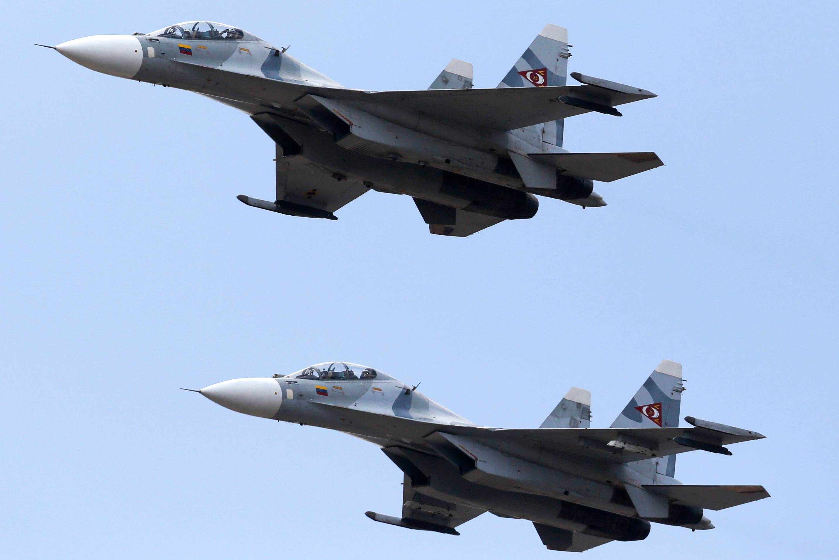Two grey Sukhoi fighter jets flying vertically adjacent on a blue sky backdrop