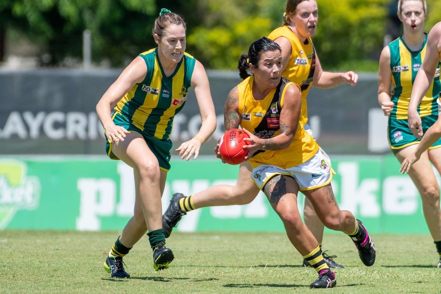 Two players run across the footy field during the day in the Northern Territory.