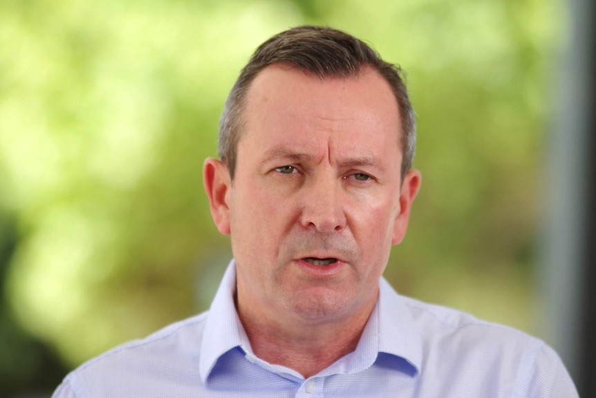 Premier Mark McGowan in blue shirt talking in front of soft green background briefing reporters on coronavirus measures