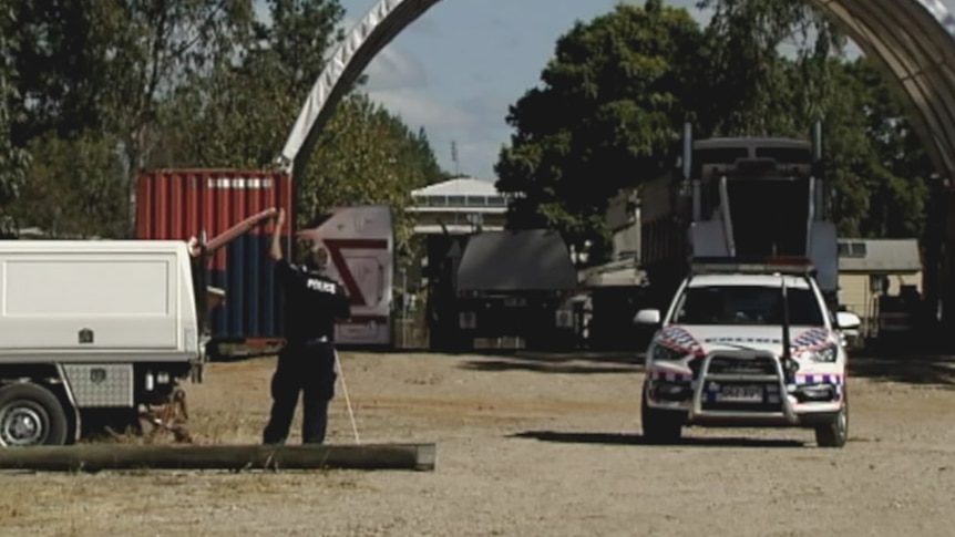 A police officer holding open the boot lid of a covered ute in a dirt car park