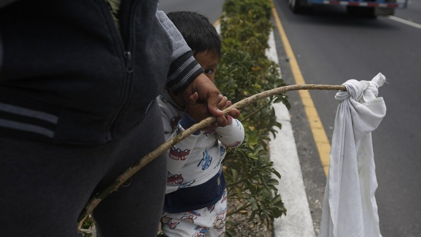 Leidy and her two-year-old son Leiton wave a white flag on la carretera al Pacifico in Villa Nueva, Guatemala.