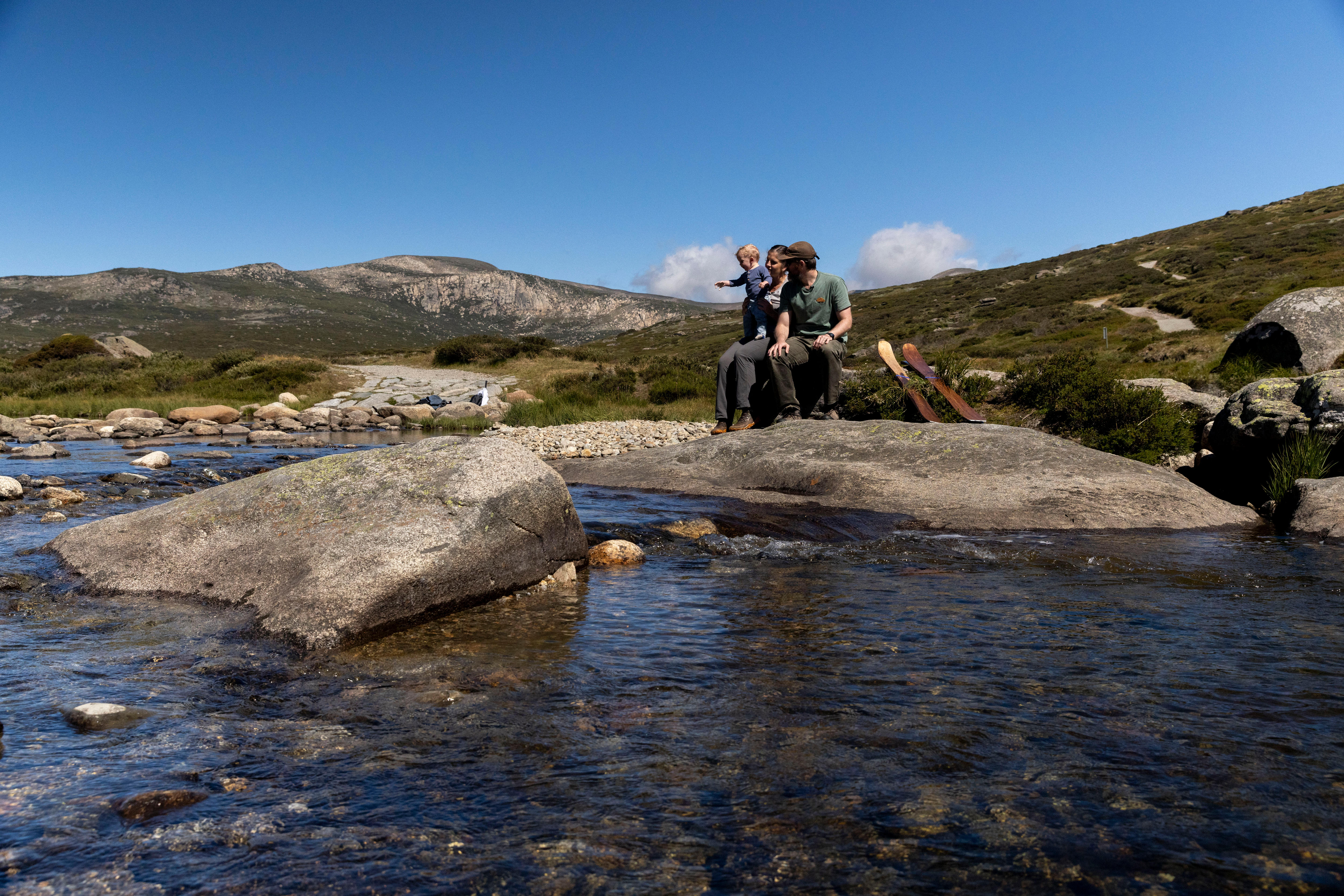 A family sitting near a stream in a green mountain. 