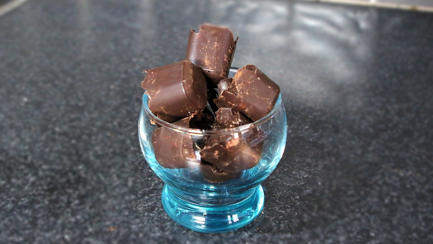 Rectangular chocolates piled up in a blue, glass cup on a kitchen bench. 