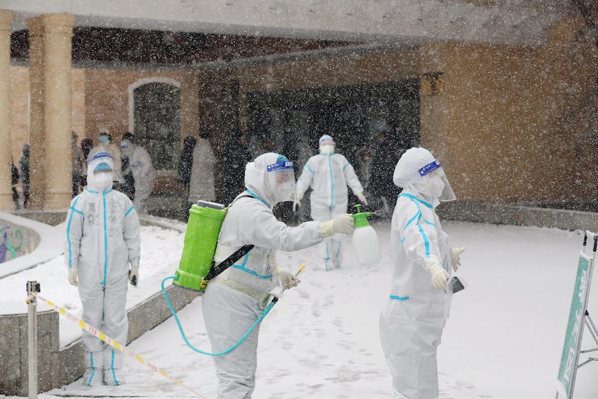 A worker in protective suits sprays another worker outside a clinic.