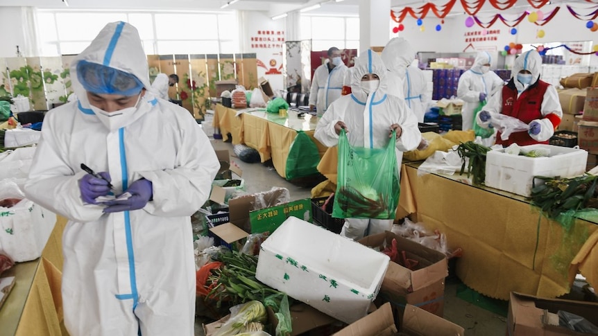 People in PPE gowns, face masks, and goggles pack food into polystyrene boxes in a brightly-coloured supermarket.