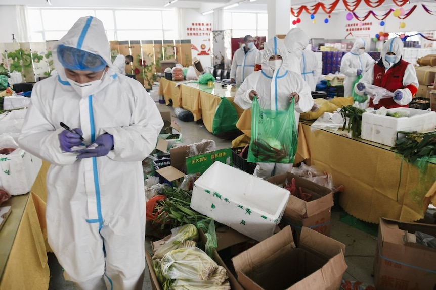 People in PPE gowns, face masks, and goggles pack food into polystyrene boxes in a brightly-coloured supermarket.