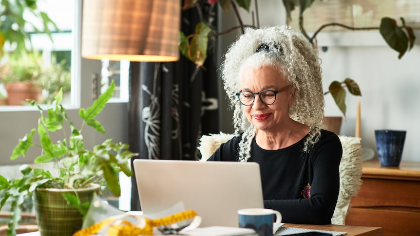 Grey haired woman at home smiling in front of laptop