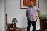 A smiling Aboriginal man in a shirt standing in front of and next to some Aboriginal art