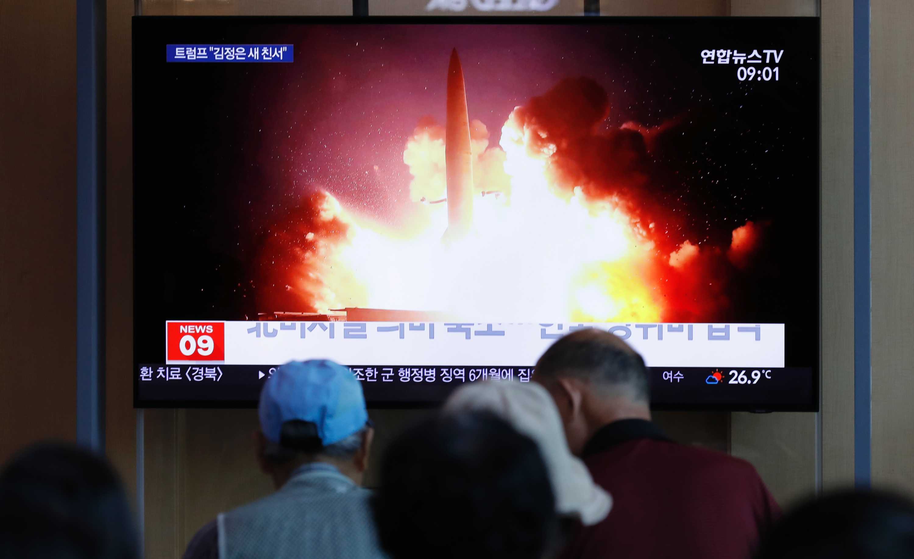 A large TV screen showing a missile taking off with Korean text, and people watching.