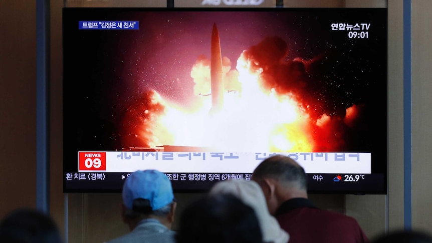 A large TV screen showing a missile taking off with Korean text, and people watching.