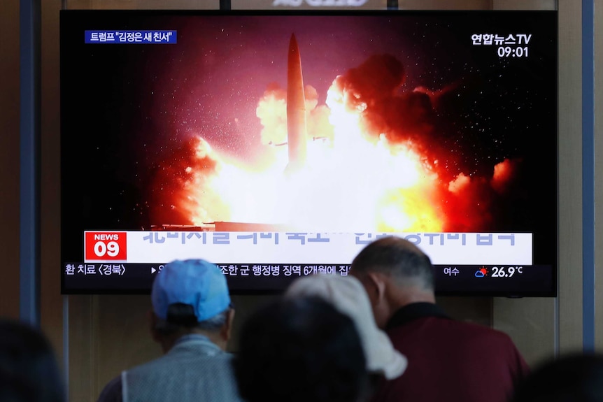 A large TV screen showing a missile taking off with Korean text, and people watching.