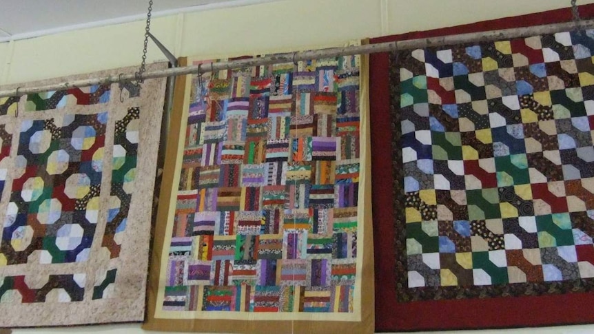 Three quilts hanging on display with brightly coloured geometric patterns.