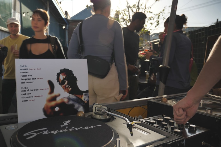 The album cover for OMC's New Urban Polynesian, with a DJ playing the vinyl record and a crowd enjoying the music.