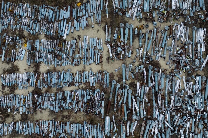 A huge mass of blue metal cylinders lie in rows in a junkyard.