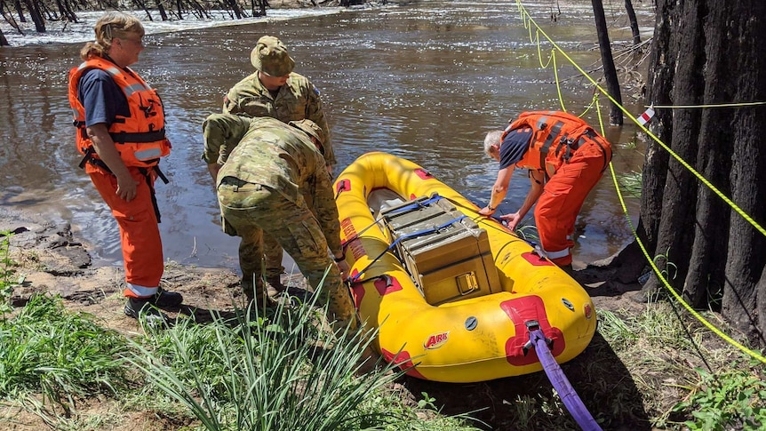 People looking at a yellow boat laden with supplies about to cross a river