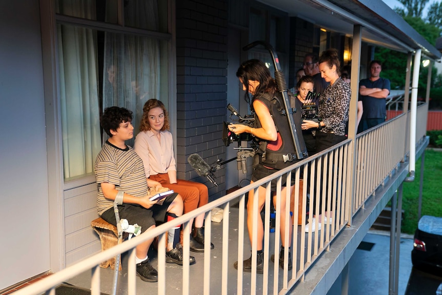 Will sits on a bench with his co-star, the film crew around them and filming them.