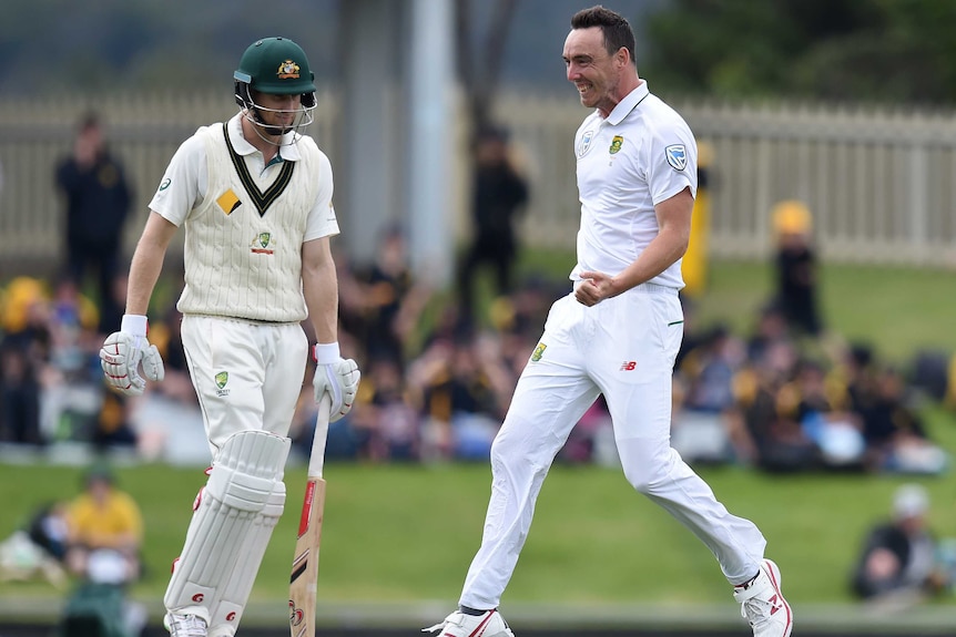 An Aussie batsman walks after being dismissed by a South African bowler. An out-of-focus crowd sits on the ground beyond