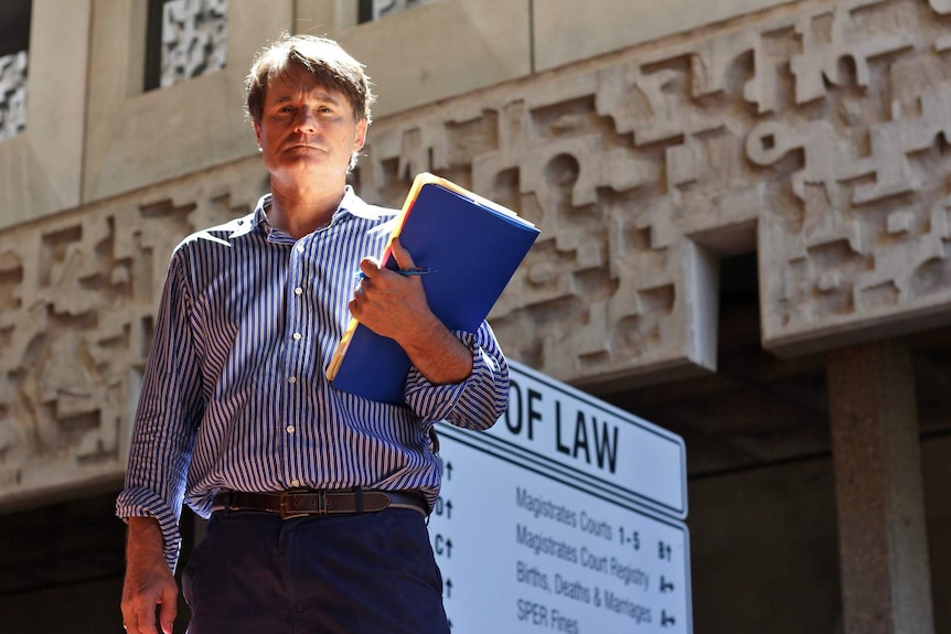 A man holds a folder while standing outside the Townsville law courts