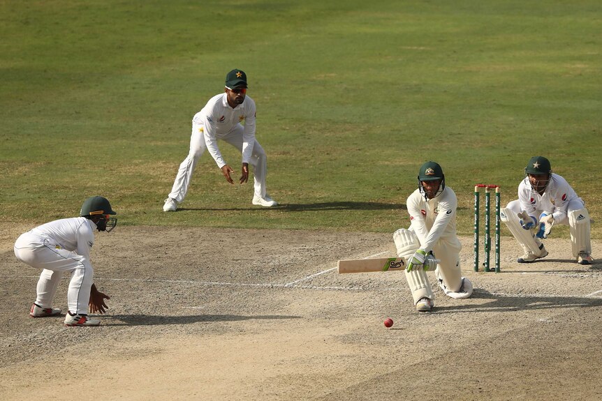 Wide shot of a cricket batsman playing a shot with fielders around.