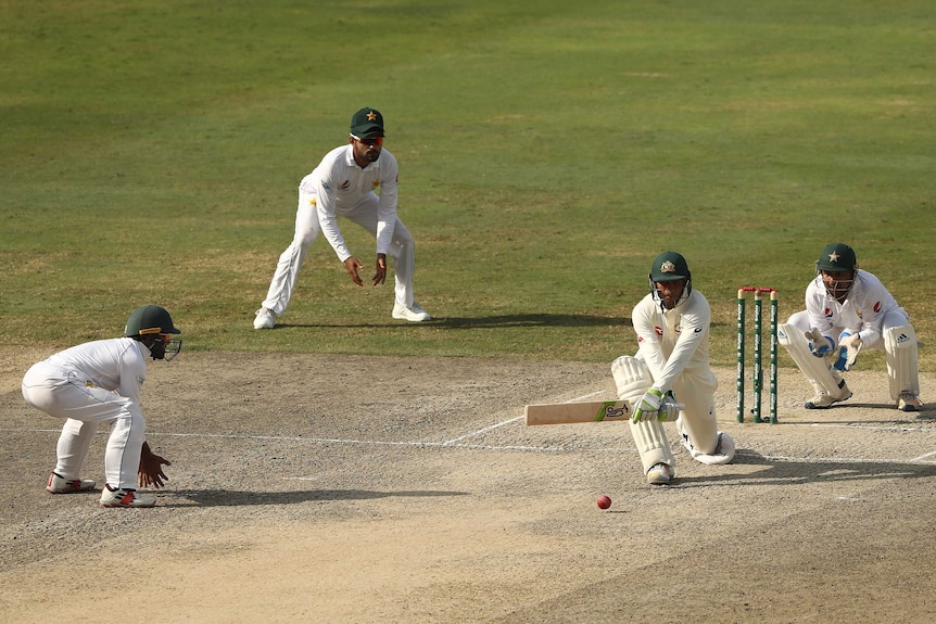 Wide shot of a cricket batsman playing a shot with fielders around.