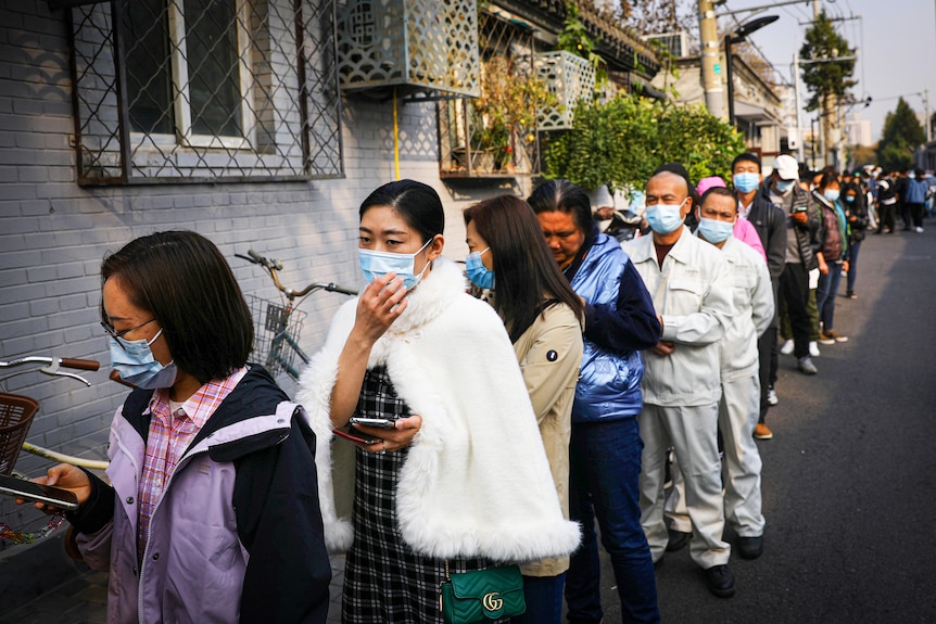 A line of people wearing blue medical face masks on a street in Beijing