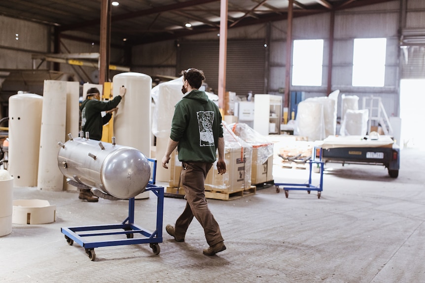 A young man walks across a manufacturing business floor while wearing a mask.