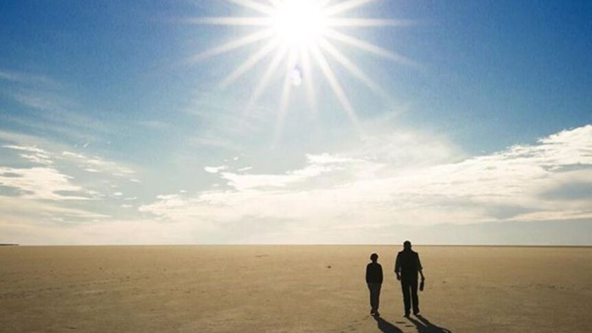 Two people walk across a dry salt lake