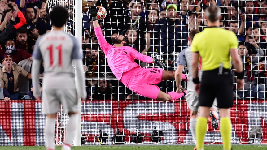 A goalkeeper flies through the air, his hand grasps at a ball that goes past him into the net.