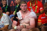 A Dolphins NRL player sits on the bench with his injured shoulder wrapped up with plastic wrap and ice during a match.
