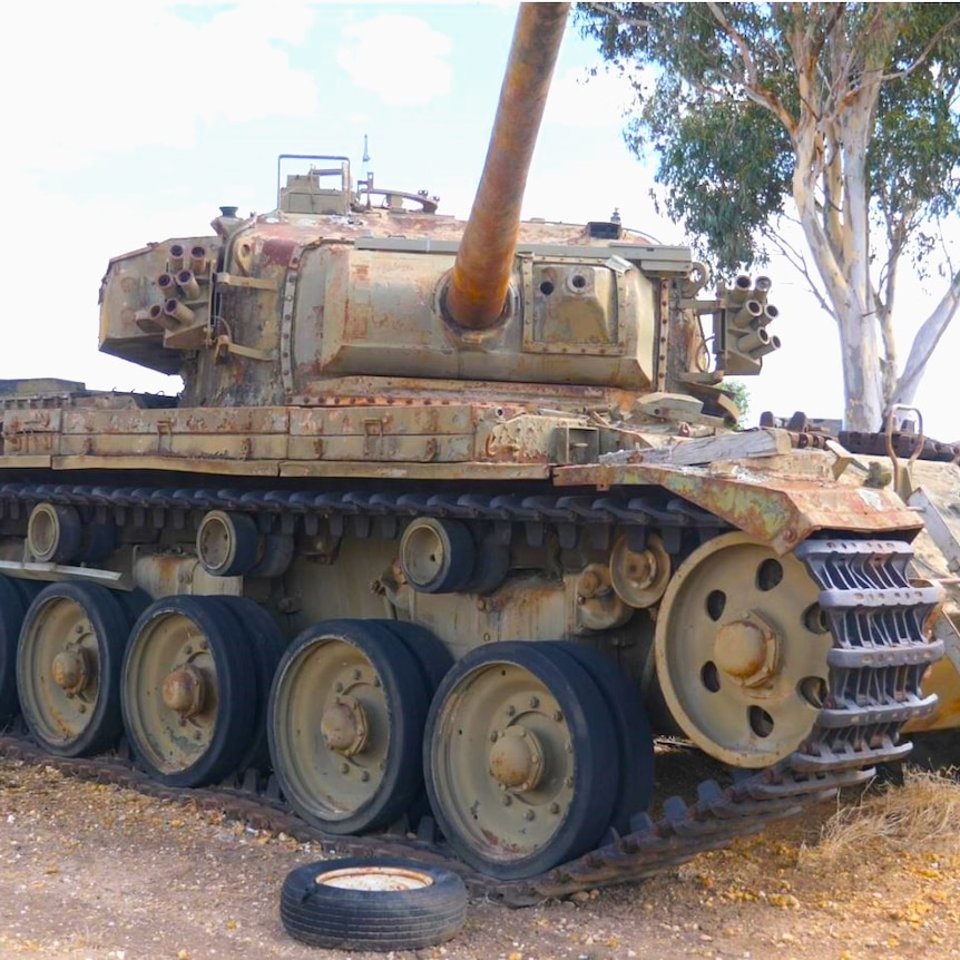A battle tank sits rusting in a yarn with a ladder up to its door and its turret open 
