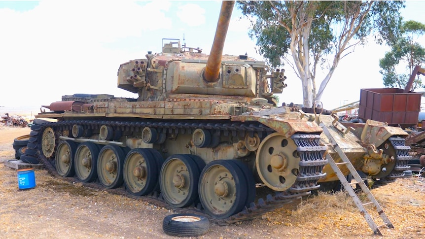 Un tanque de batalla se encuentra oxidado en un hilo con una escalera hasta su puerta y su torreta abierta 