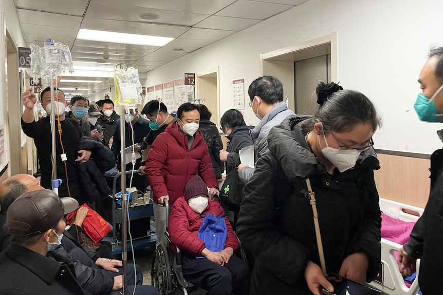 Patients crowd a hospital hallway wearing masks and holding IV drips
