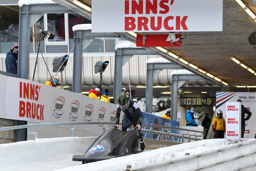 Racer running behind a bobsleigh ready to jump in and race down the icy track