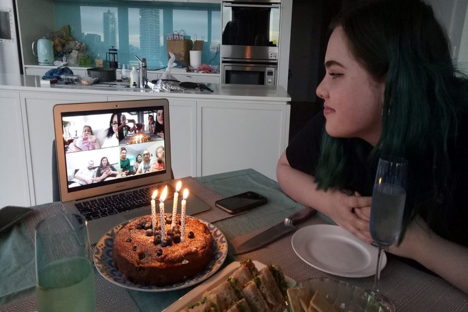 Young woman with birthday cake joined by friends on computer screen
