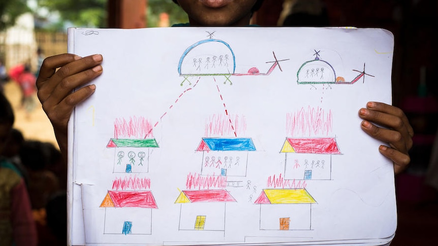 A child holds up a drawing that shows helicopters shooting people's houses.