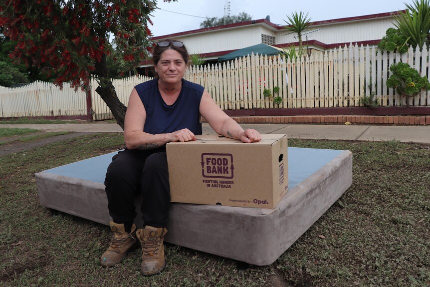 A person with a Foodbank box on a mattress outside a house. 
