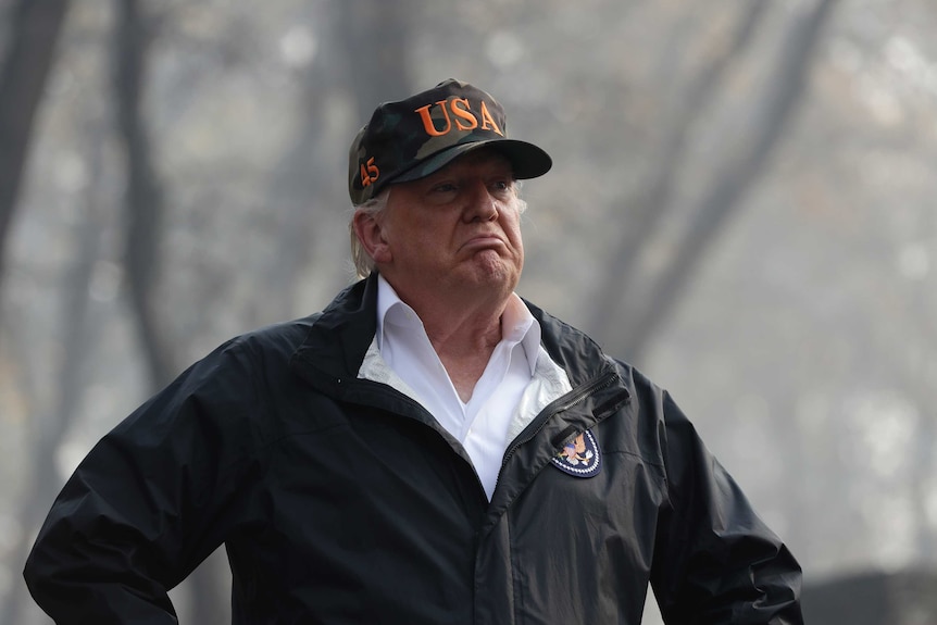 a man stands in front of trees with a hat on