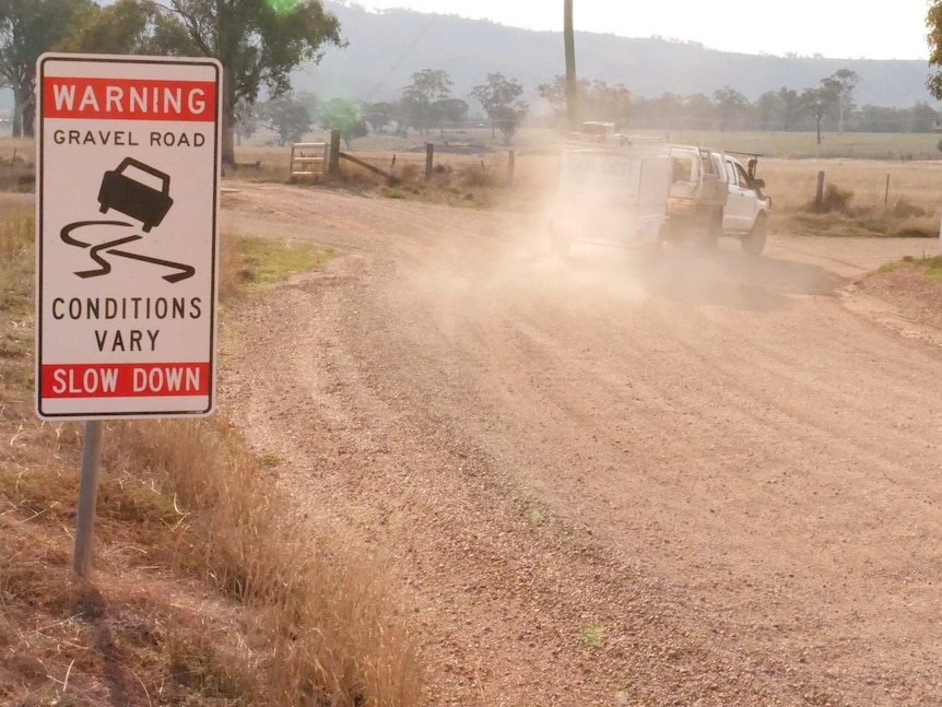 A ute drives along a gravel road and past a sign warning vehicles to slow down.